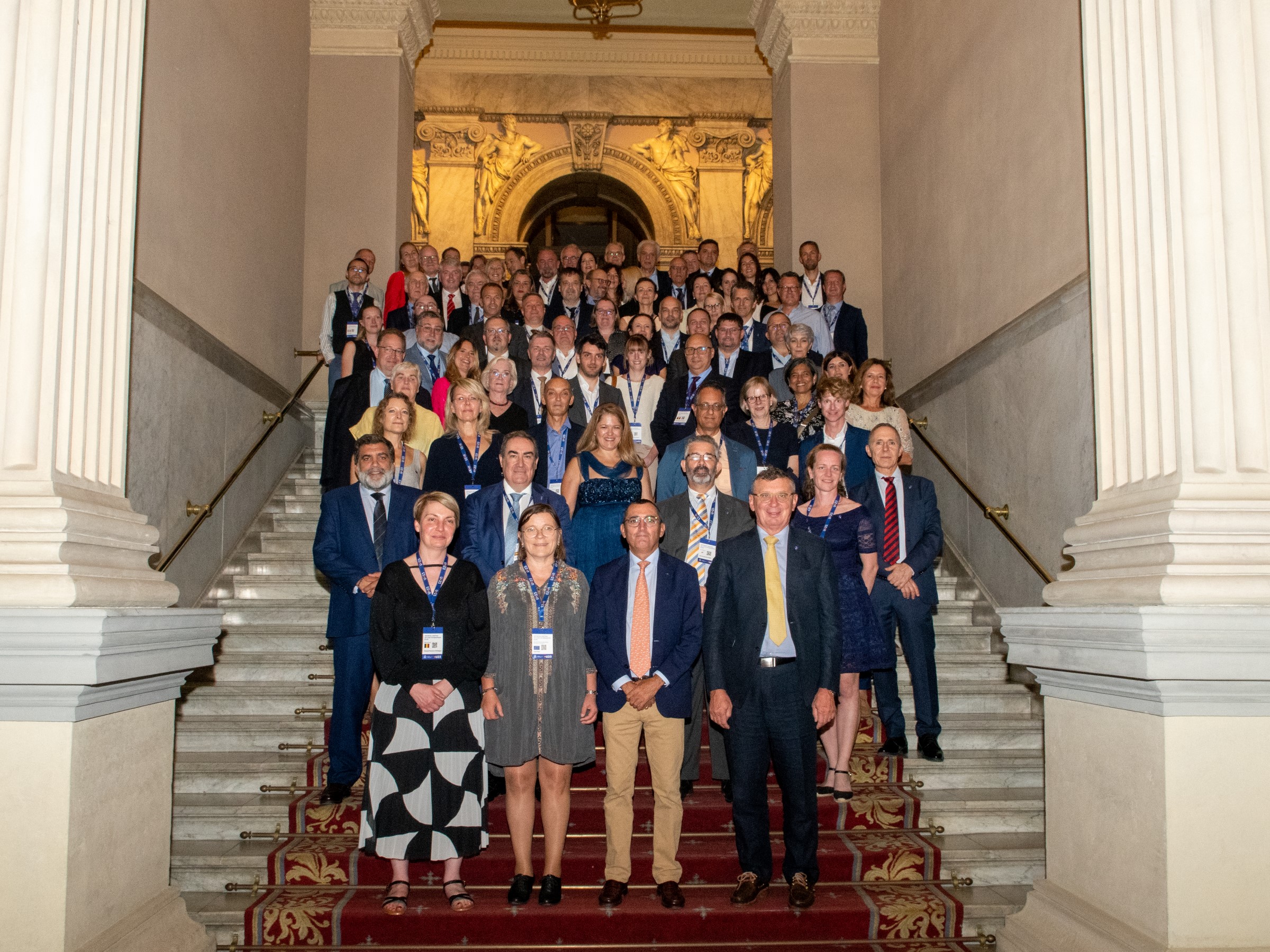 Uczestnicy posiedzenia Grupy Roboczej Głównych Lekarzy Weterynarii państw członkowskich UE w Madrycie na tle schodów w dużym budynku po bokach dwie białe kolumny 